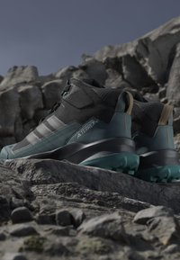 Fodtøj til vandring med sort overdel, netpaneler, teal accenter, tyk gummisål, robust sålkonstruktion og forstærket hæl.