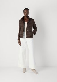 Veste matelassée marron avec un col haut, des boutons sur le devant et des poches latérales, associée à un haut blanc ajusté et un pantalon large blanc.