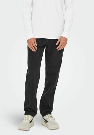Zwarte jeans met een rechte snit, met een gladde textuur. Gecombineerd met een wit shirt met lange mouwen en lichtgekleurde sneakers.