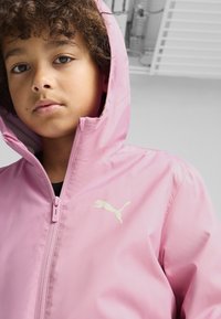 Rožinė vandeniui atspari striukė su gobtuvu, kurią papildo baltas Puma logotipas ant krūtinės ir užtrauktuko uždarymas, pagaminta iš sklandžios, lengvos medžiagos.