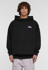 Melna kapuce ar priekšējo kabatu un auklu kapuci. Ar rozā logo augšējā kreisajā krūtīs. Materiāls izskatās mīksts.