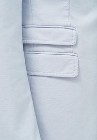 Světle modrá texturovaná látka zblízka se strukturovaným střihem a dvěma vodorovnými kapsami se šitými detaily.