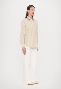 Beige stripete skjorte med lange ermer, kombinert med hvite vide bukser og beige slip-on sko. Glatt stofftekstur, avslappet passform.