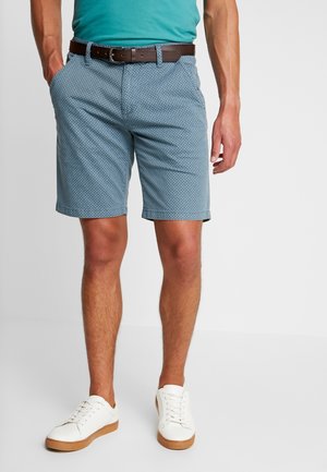 Shorts pour hommes bleus à motif, fabriqués en tissu léger, avec une coupe classique, des poches latérales et une ceinture en cuir marron. Portés avec des baskets blanches.