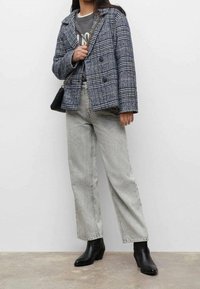 Karierte Wollmischungjacke mit doppelten Knöpfen in Grau- und Blautönen. Kombiniert mit hochgesprochenen, hellgrauen Jeans und schwarzen Ankle Boots.