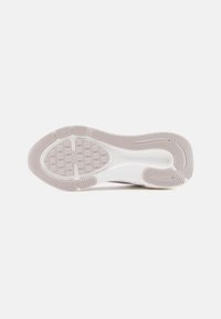 Σόλα λευκού αθλητικού παπουτσιού με υφασμένα σχέδια πρόσφυσης και αυλάκια για πρόσφυση σε απλό φωτεινό φόντο.