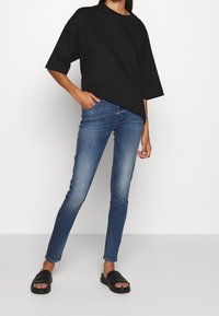 Black oversized t-shirt, medium weight cotton, relaxed fit. Light blue slim-fit jeans, denim material. Black slide sandals with a smooth finish.