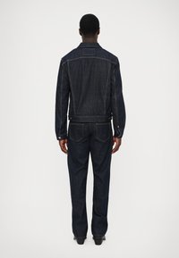 Chaqueta de mezclilla azul oscuro y jeans a juego. La chaqueta presenta un corte entallado, detalles de botones y un parche en la parte trasera. Textura suave con un desgaste mínimo.