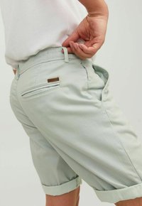 Světlé zelené kostičkované šortky s hladkým povrchem, které mají zadní kapsu a ohrnuté nohavice. Vyrobené z prodyšné tkaniny.