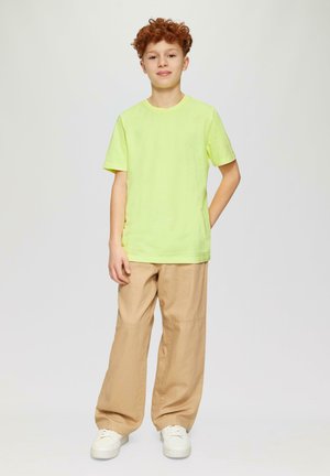 Limoengroene korte mouwen t-shirt gecombineerd met losse beige broek en witte sneakers, met een ontspannen fit en eenvoudig ontwerp.