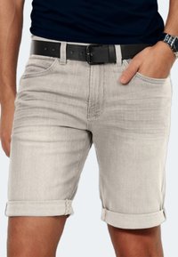 Hellgraue Jeansshorts mit klassischem Schnitt, umgeschlagenen Säumen und Vordertaschen. Getragen mit einem schwarzen Gürtel. Texturiertes Gewebe mit sichtbaren Nähten.