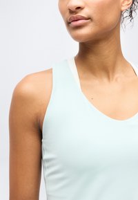 Κοντινό πλάνο ενός ατόμου που φοράει ανοιχτό μπλε αμάνικο τοπ με ορατό λευκό ιμάντα από κάτω, δείχνοντας τον λαιμό, τον ώμο και τα χείλη του.