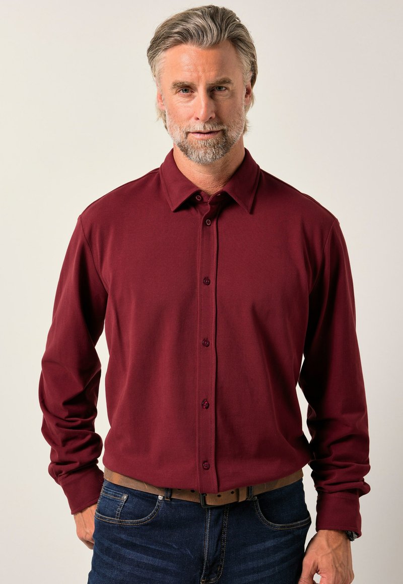 Camicia a maniche lunghe bordeaux con colletto button-down, bottoni frontali e una texture liscia, abbinata a jeans blu scuro e una cintura.