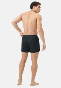 Pantaloni da bagno neri con vita elastica, caratterizzati da fessure laterali e un materiale leggero. Il modello è posato di schiena.