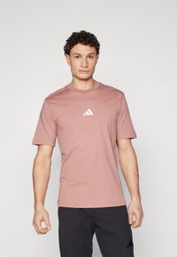 Korte mouwen, lichtroze katoenen t-shirt met een ronde hals en witte logodetail op de borst; gecombineerd met donkere broeken.
