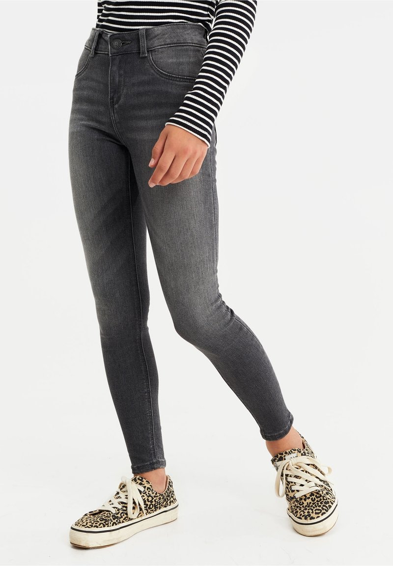 Person med urtvättade svarta slim-fit jeans, svartvit randig långärmad tröja och leopardmönstrade sneakers med vita snören.