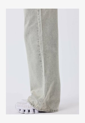 Helle graue Denim-Jeans mit geradem Schnitt, ausgestattet mit einer sauberen Verarbeitung und seitlichen Nähten, kombiniert mit weißen Sportschuhen.