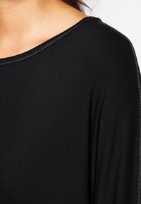 T-shirt nera con scollatura ampia, texture liscia e dettagli di cucitura sottili lungo i bordi. Il tessuto appare leggero e si drappeggia dolcemente.