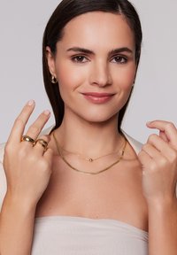 Złota biżuteria zawiera naszyjnik z warstwami z okrągłym zawieszką oraz dwa pierścionki o gładkich, zaokrąglonych kształtach. Kolczyki to okrągłe obręcze.