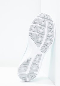 Bílá sportovní podešev boty s texturovaným gripem, obsahující obdélníkové a šestihranné důlky. Hladký gradientní design na okrajích.
