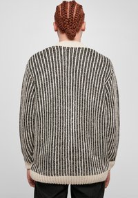 Pull en tricot avec des rayures verticales noires et blanches, manches longues, coupe décontractée, et un col et un ourlet côtelés. Tissu texturé avec de la profondeur.