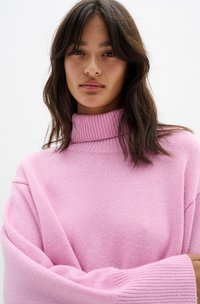 Maglione a collo alto di un rosa chiaro con vestibilità ampia, colletto a coste e maniche oversize. Tessuto morbido con un motivo lavorato a maglia su tutta la superficie.