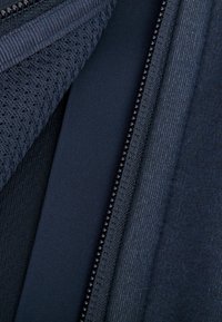 Marineblaue Stoffmuster mit verschiedenen Texturen: gestrickt, glatt und gerippt, mit einem Reißverschluss-Detail, das kleine schwarze Nieten entlang der Kante zeigt.