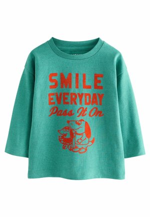Türkiser langärmliger Sweatshirt mit rotem Text "SMILE EVERYDAY Pass It On" und darunter abgebildeten Cartoon-Hunden. Weicher Stoff, runder Ausschnitt, lockere Passform.