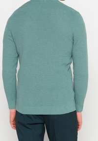 Suéter de punto en color verde azulado suave con un patrón texturizado. Cuenta con mangas largas y un dobladillo acanalado, diseñado para una silueta ajustada.