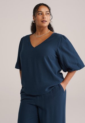 Top blu navy con scollo a V, maniche corte a sbuffo e vestibilità morbida. Realizzato in tessuto leggero e strutturato. Modello indossa pantaloni blu navy coordinati.