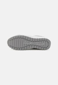 Hvite sneakers med en teksturert grå gummisåle som har et stripet mønster. Merkevaren visible på mellomsålen.