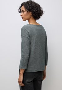 Randig, lätt top i mörkgrön och grå, med vid halsringning och trekvartslånga ärmar, samt texturerade axelaccenter.