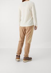 Långärmad, krämfärgad skjorta med mjuk textur, matchad med bruna byxor med ljusbruna accenter och sned panelering. Bruna vandringskängor.