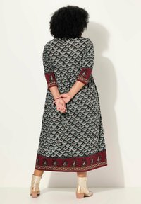 Lång svart klänning med intrikata teal blommönster, vinröda ärmar och en dekorativ fåll. Har en smickrande A-linjeform.