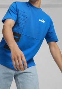 Modrá bavlněná tričko s výraznou černou grafikou a logem "PUMA" na hrudi. Krátké rukávy a design s kulatým výstřihem.