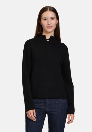 Maglione nero lavorato a maglia con un collo alto e un piccolo taglio decorativo. Maniche lunghe, texture a costine e una vestibilità morbida. Abbinato a jeans scuri.