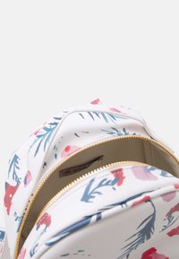 Plecak w kwiatowy wzór z białą, fakturowaną powierzchnią, złotym zamkiem błyskawicznym i dwiema przegrodami; zdobiony niebieskimi i czerwonymi kwiatami oraz liśćmi.