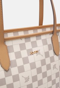 Ljust beige handväska med rutmönster. Släta lädermaterial, kontrasterande bruna handtag och en guldig logotypaccent på framsidan.