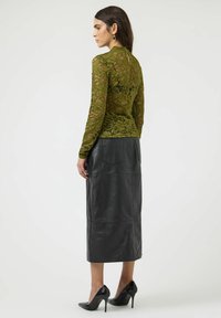 Zielona bluzka z długim rękawem z koronką zdobiona kwiatowymi wzorami, w połączeniu z czarną, midi spódnicą ze skóry; modelka ma na sobie czarne buty na wysokim obcasie.