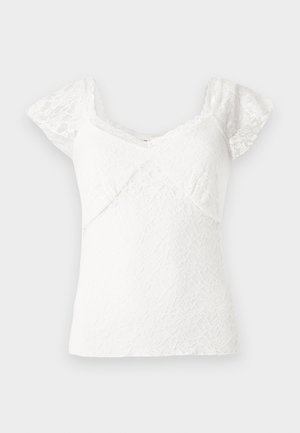 Top din dantelă albă cu mâneci scurte tip capă, având un decolteu în V și un model floral texturat pe întreaga suprafață. Material neted cu margini unde se termină în ondulații.