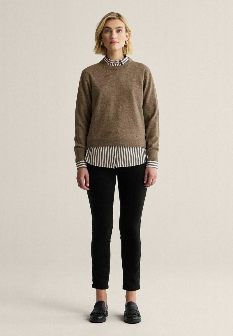 Brun tröja över en vit och grårandig skjorta, tillsammans med svarta slim-fit byxor och svarta skor. Slät textur och enkel design.