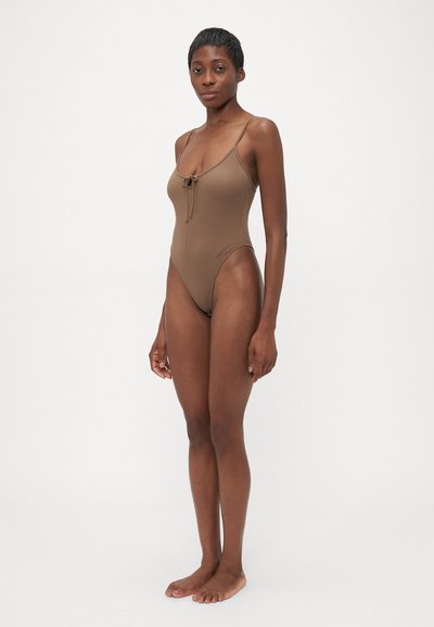 Maillot de bain en une pièce marron à côtes avec des bretelles spaghetti réglables, décolleté plongeant et détail à nouer à l'avant. Ouverture de jambe haute.