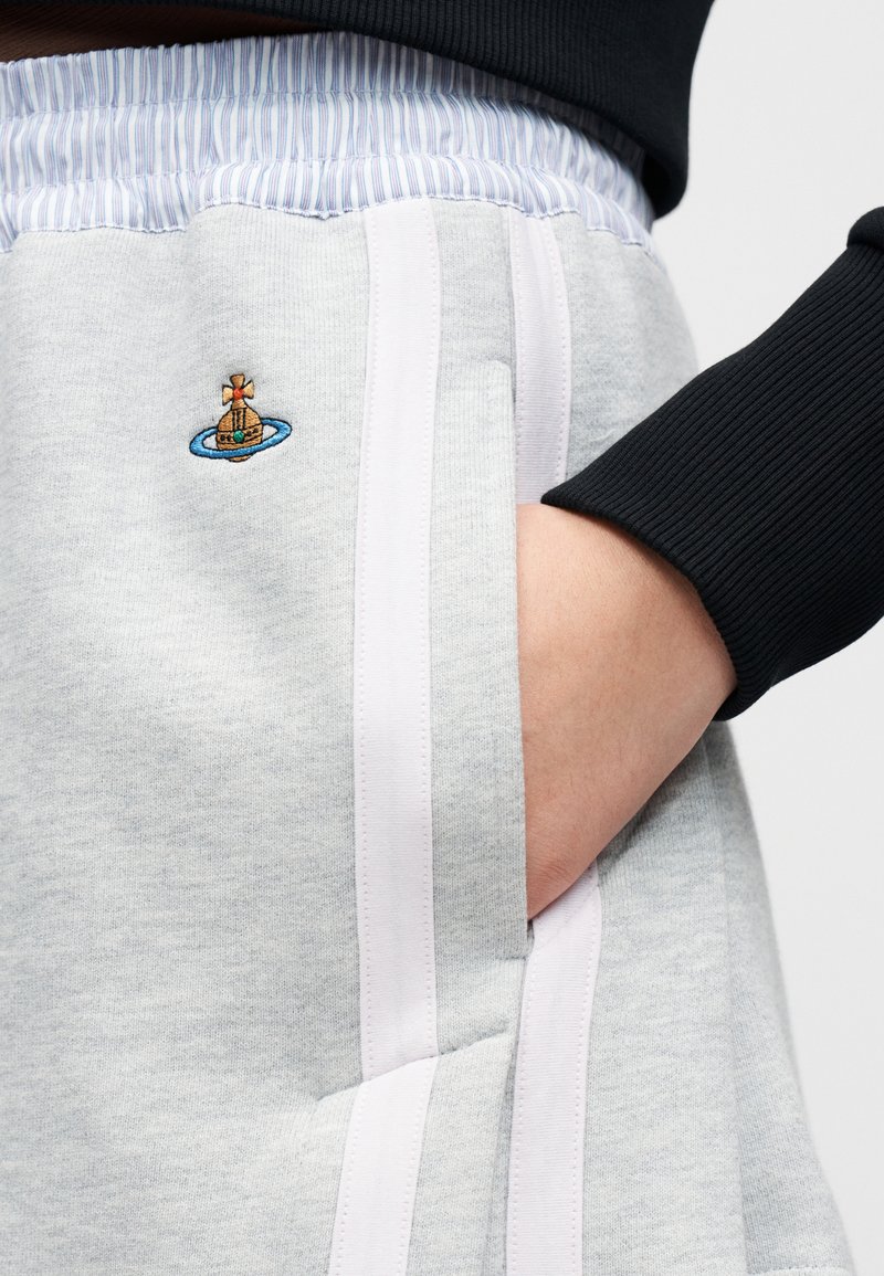 Pantalon de survêtement gris clair avec une texture douce, bandes blanches sur les côtés, et un dessin brodé coloré d'un navire sur un cercle bleu.