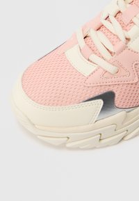 Jasnoróżowy tenisówka z siateczkową cholewką i kremowymi skórzanymi akcentami. Posiada grubą, teksturowaną podeszwę oraz cienkie białe sznurówki zapewniające pewne dopasowanie.