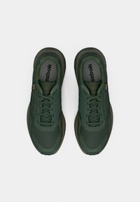 Par de sapatilhas verdes da Reebok com atacadores, textura de malha e camurça, vistas de cima sobre um fundo branco.