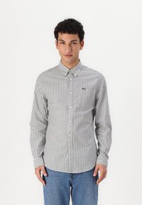 Button-up shirt in striped grey and white fabric, featuring a collar, long sleeves, and a chest pocket with a small logo.