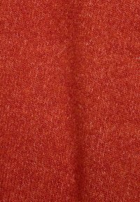 Gros plan d’un tissu tricoté rouge-orange doux et texturé avec des motifs de tissage visibles et de légères variations de couleur.