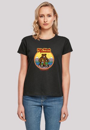 Frau trägt ein schwarzes T-Shirt mit einer bunten Illustration von zwei Kindern und einem Bären vor Bergen, mit dem Text "Freunde schließen im Yellowstone-Nationalpark."