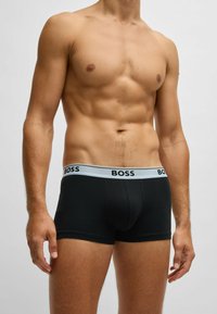 Schwarze Boxershorts mit einem hellblauen Bund, der das "BOSS"-Logo in Schwarz trägt. Hergestellt aus einem glatten, dehnbaren Material.