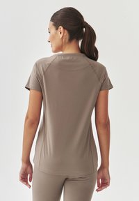 Korte mouwen, lichtbruine sporttop met een soepele textuur en een gebogen naaddetail aan de achterkant. Ontworpen voor comfort en flexibiliteit.